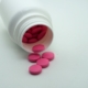 View of pink-coated tablets falling out of a medicine bottle